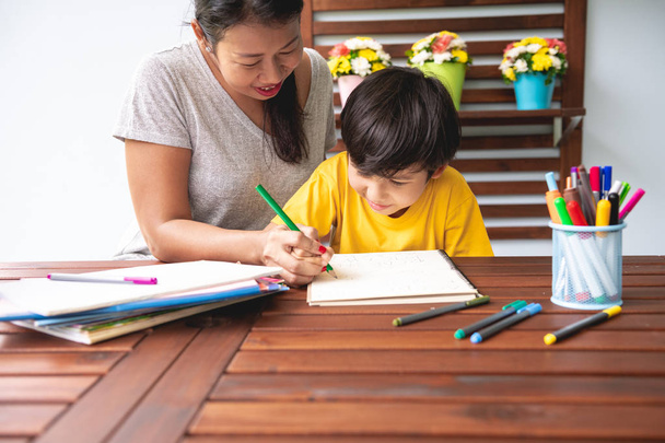 Children homework. Young mixed race boy doing homework in terrace at home with his mother teaching him. Writing practice. Happy mood. Back to school concept. - 写真・画像