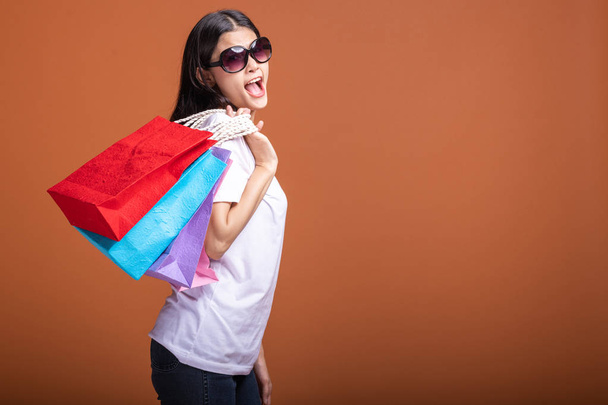 Woman holding shopping bag isolated in orange background. Young asian woman in white t-shirt, happy mood. Shopping concept. - Foto, Imagem