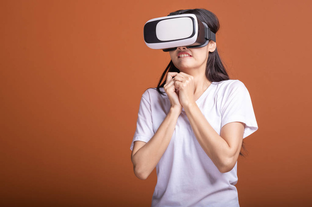 Woman wearing VR headset. Young Asian woman in white t-shirt with VR head gear, shocking scare pose. New entertainment concept. - Фото, зображення