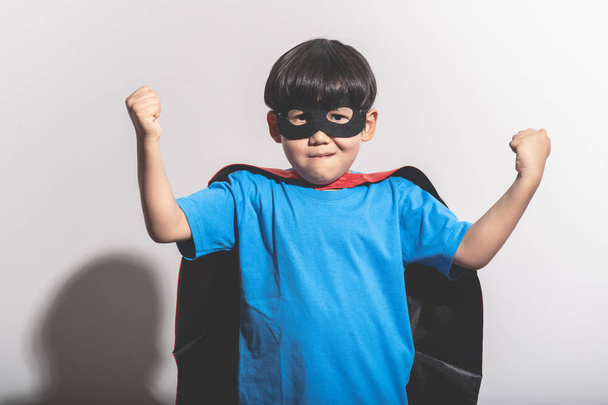Young boy super hero portrait in white background with hard light. Mixed race boy in blue shirt, jean, mask, cape. Powerful pose. - Foto, Imagen