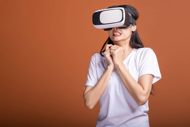 Woman wearing VR headset. Young Asian woman in white t-shirt with VR head gear, shocking scare pose. New entertainment concept. - Zdjęcie, obraz