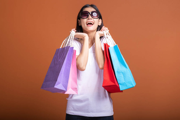 Woman holding shopping bag isolated in orange background. Young asian woman in white t-shirt, happy mood. Shopping concept. - Photo, Image