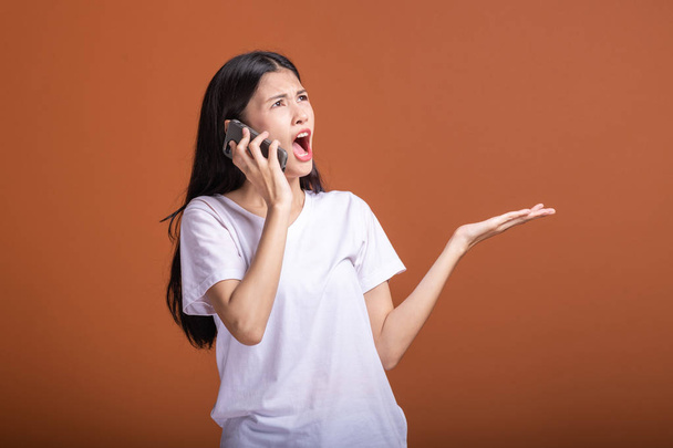 Woman using mobile phone isolated over orange background. Asian woman in white t-shirt, shock pose, open palm. Hipster life style concept. - Photo, Image