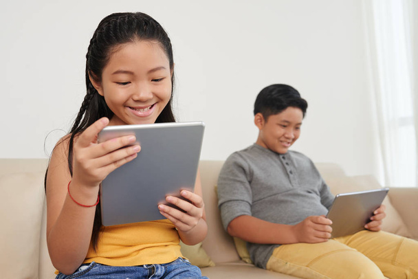 zwei asiatische Kinder zu Hause auf dem Sofa, Kinder surfen auf digitalen Tablets  - Foto, Bild