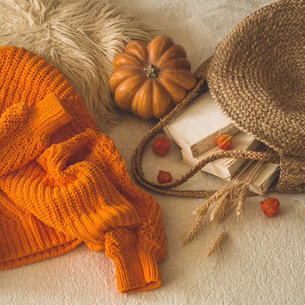 Gezellige gebreide warm oranje trui met oude boeken en vintage stro tas op witte warme plaid met pompoen, physalis, boeken lezen - Foto, afbeelding