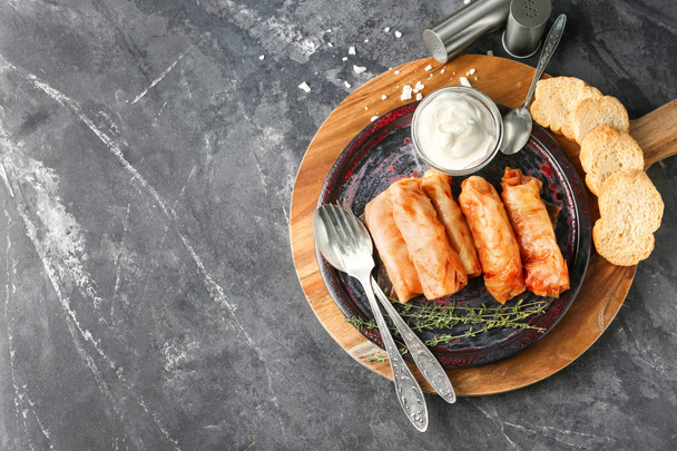 Plate with stuffed cabbage leaves and bowl of sour cream on wooden board - Foto, immagini