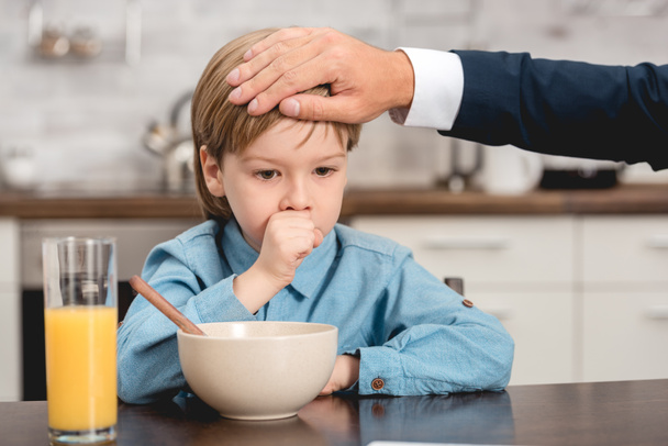 cropped shot of father checking temperature of son with hand during breakfast - Photo, Image