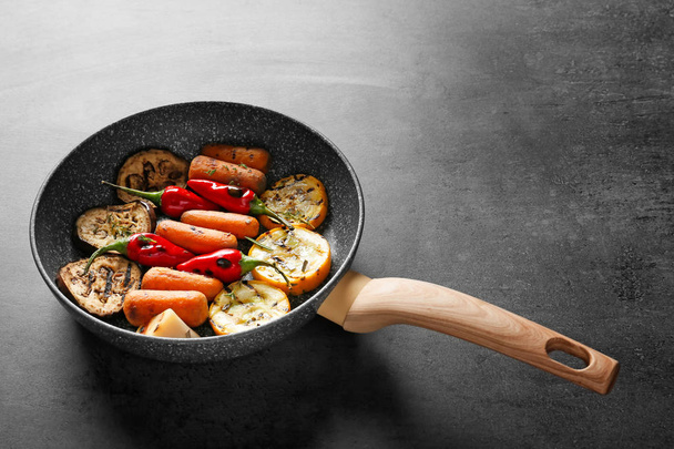 Τηγάνι με νόστιμα ψητά λαχανικά σε γκρίζο πίνακα - Φωτογραφία, εικόνα