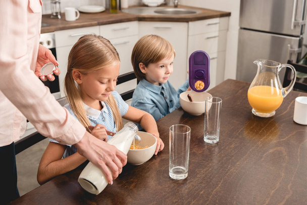 περικοπεί πλάνο της μητέρας ρίχνει το γάλα στα δημητριακά για αξιολάτρευτο λίγο τα παιδιά κατά τη διάρκεια του πρωινού - Φωτογραφία, εικόνα