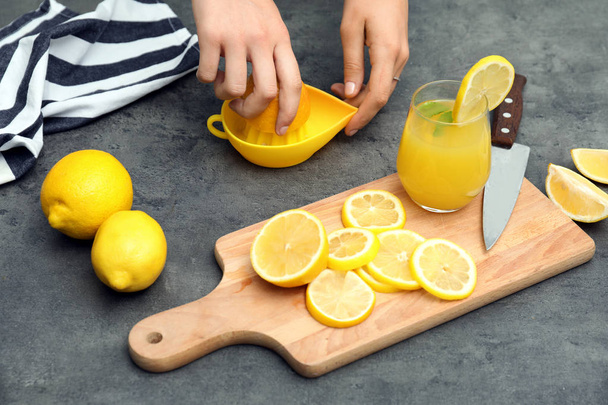 Woman preparing fresh lemon juice on grey table - Foto, imagen