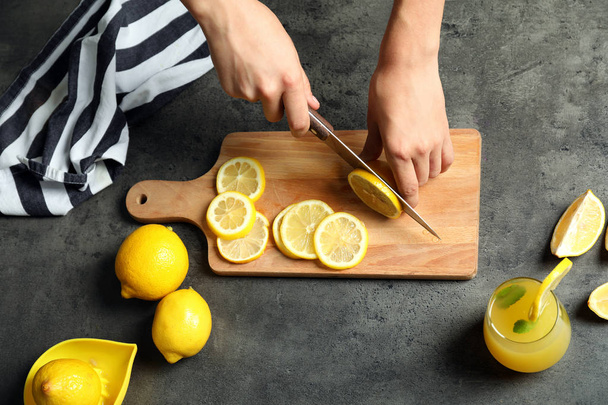 Woman cutting fresh lemon for juice on grey table - Photo, image