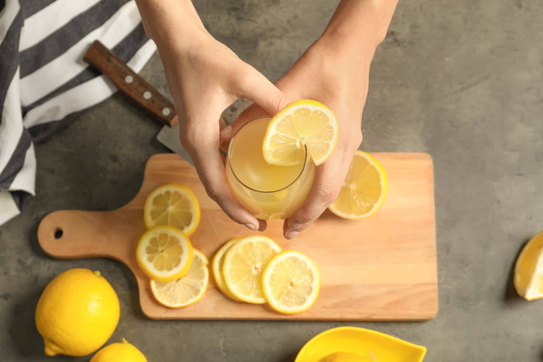 クローズ アップ テーブルに新鮮なレモン ジュースのガラスを保持している女性 - 写真・画像