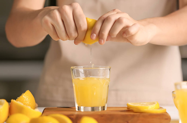 Woman squeezing fresh lemon juice into glass at table - Fotoğraf, Görsel