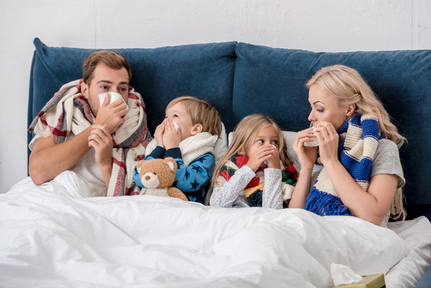 malato giovane famiglia soffiando nasi con tovaglioli insieme mentre sdraiato a letto e guardando l'un l'altro
 - Foto, immagini