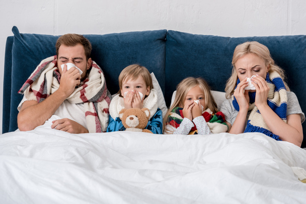 sick young family blowing noses with napkins together while lying in bed - Photo, Image