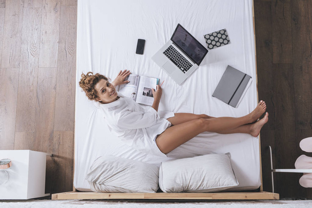 Z góry zdjęcie kobiety pracy na jej laptopie i siedzi na łóżku. - Zdjęcie, obraz