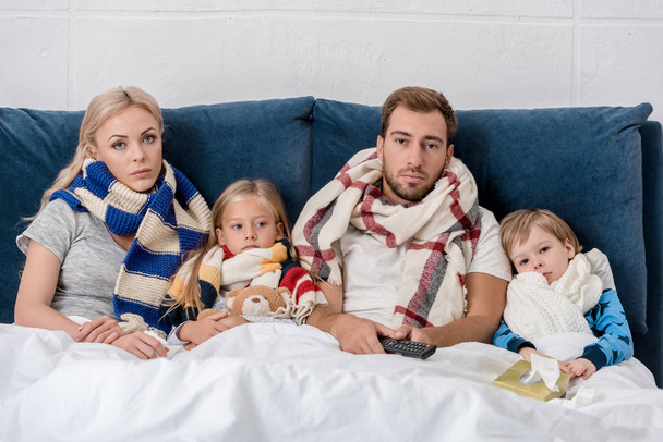 Kranke junge Familie in Schals blickt im Bett in die Kamera - Foto, Bild