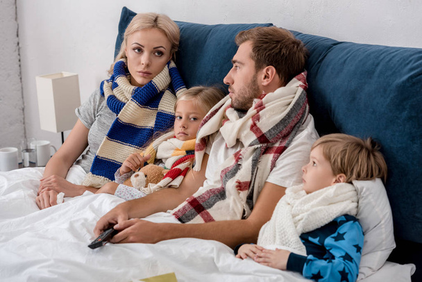 sick young family in scarves looking at each other while lying in bed - Photo, Image