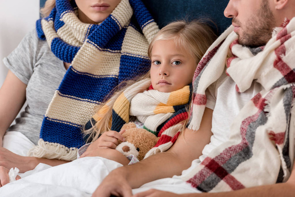 крупним планом портрет маленької хворої дитини лежить в ліжку з батьками в шарфах
 - Фото, зображення