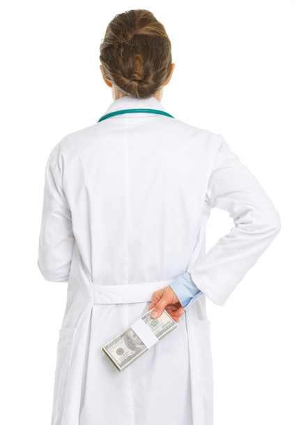 Medical doctor woman hiding pack of dollars behind back - Valokuva, kuva