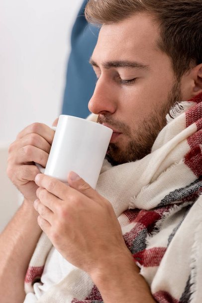 close-up portrait of sick young man in scarf with cup of tea - Fotoğraf, Görsel