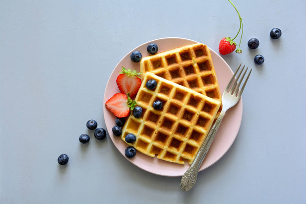 Belgian waffles with strawberries and blueberries on pink plate on gray wooden background. Top view. Copy space - Фото, зображення