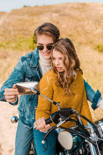 junges Paar blickt in Spiegel eines Oldtimer-Motorrads - Foto, Bild