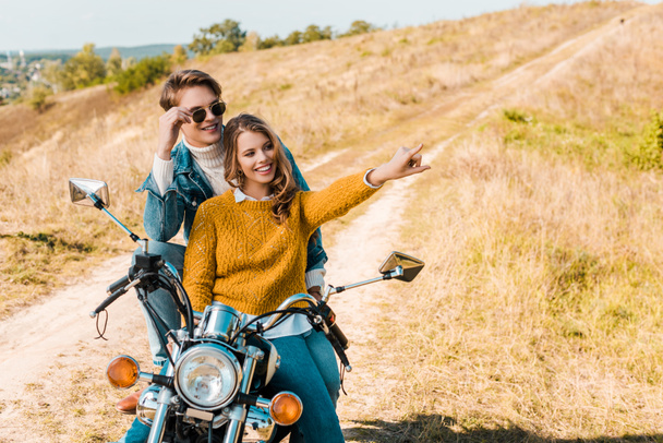happy couple sitting on motorbike and girlfriend showing something   - Zdjęcie, obraz
