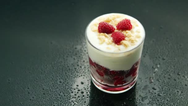 From above glass of yogurt dessert with raspberry, jam and granola on dark table with condensation  - Footage, Video