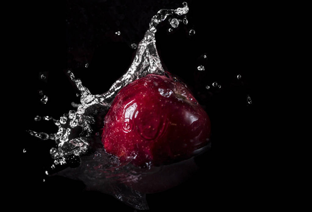 Una manzana roja cayendo en el agua con salpicadura sobre fondo negro
 - Foto, imagen