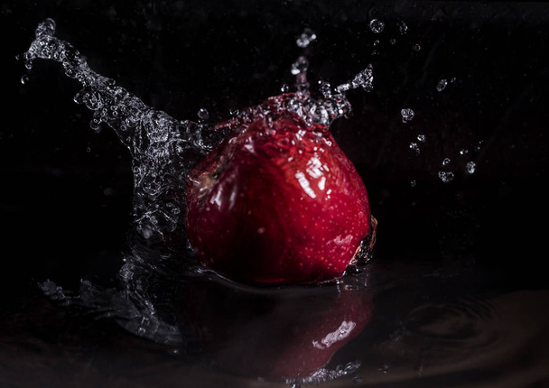 Una manzana roja cayendo en el agua con salpicadura sobre fondo negro
. - Foto, imagen