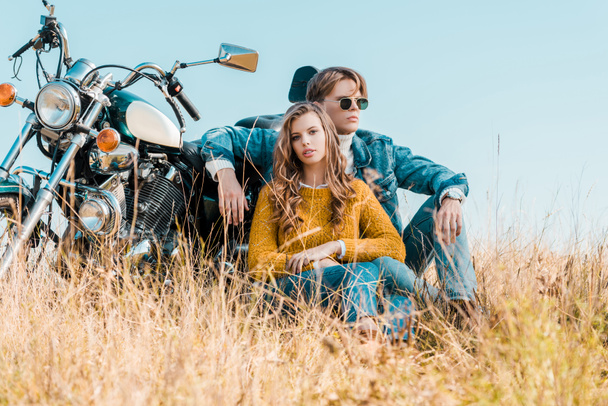 young boyfriend and girlfriend while sitting near motorbike on meadow - 写真・画像