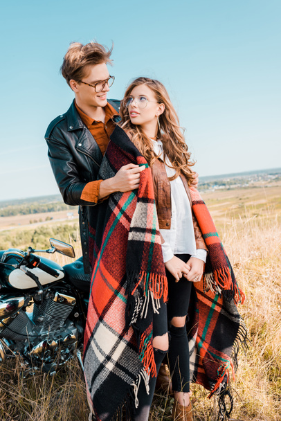 young couple in glasses standing near vintage motorbike and looking at each other - Фото, зображення