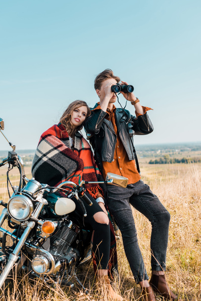 young boyfriend looking through binoculars near girlfriend sitting on motorbike  - Photo, Image