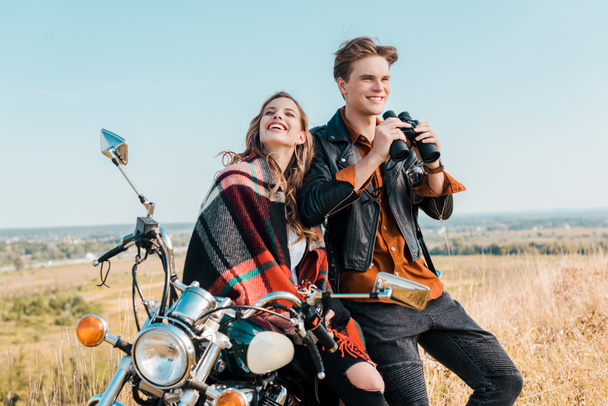 smiling boyfriend holding binoculars near girlfriend sitting on motorbike  - Photo, image