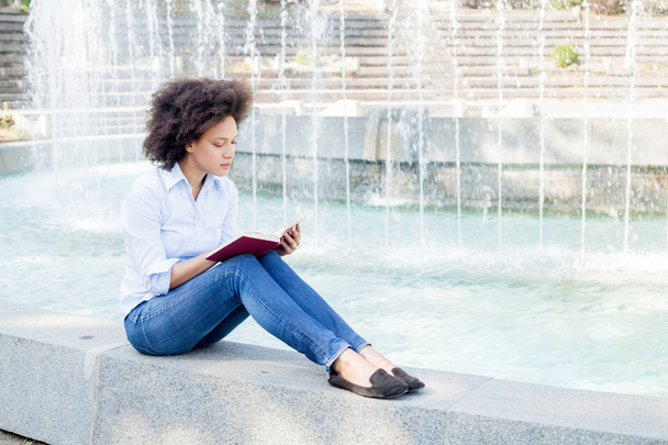 Retrato de hermosa mujer joven afroamericana leyendo el libro, atractiva raza mixta femenina relajante al aire libre, ropa casual
 - Foto, Imagen