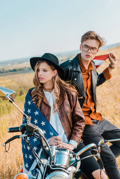 バイク、独立記念日の概念の上に座ってアメリカの国旗を持つ若いカップルします。   - 写真・画像