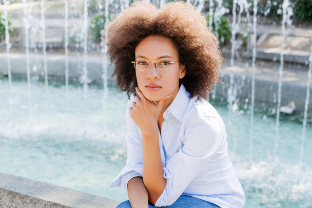 Retrato de hermosa mujer afroamericana reflexiva con gafas al aire libre, desgaste casual, mirando a la cámara
 - Foto, imagen