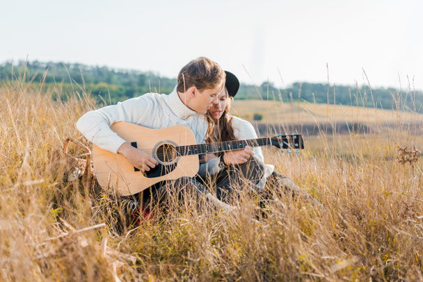 vriendje gitaarspelen in de buurt van vriendin op landelijke weide - Foto, afbeelding