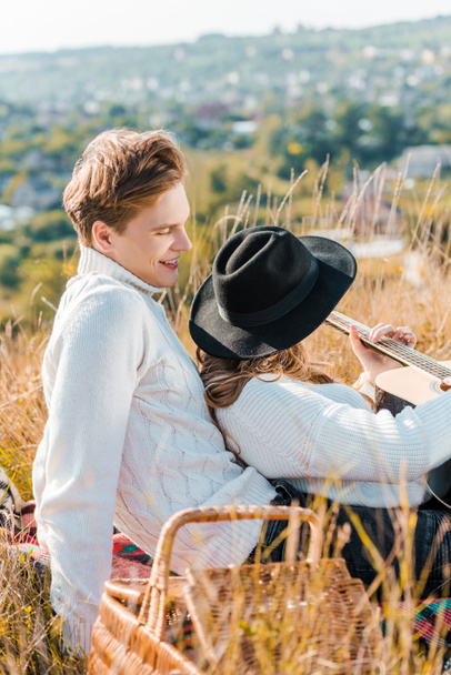 novia en sombrero negro sosteniendo la guitarra mientras su novio se relaja en la hierba
 - Foto, imagen