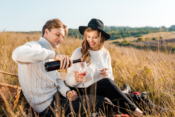 若い彼氏草原でピクニック中にガール フレンドのため赤ワインを注ぐ - 写真・画像