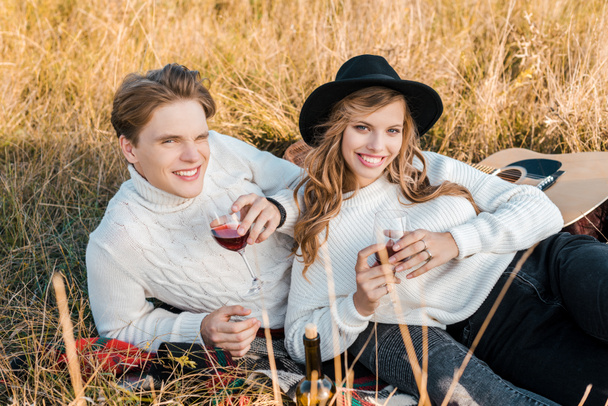 smiling couple holding wineglasses with red wine on meadow - Photo, Image