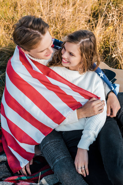 sonriente pareja con bandera americana en el picnic, concepto del día de la independencia
  - Foto, imagen