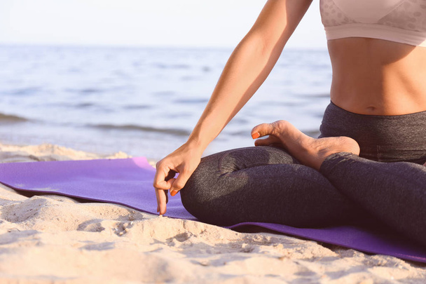 Woman practicing yoga on sea shore, closeup - Foto, afbeelding