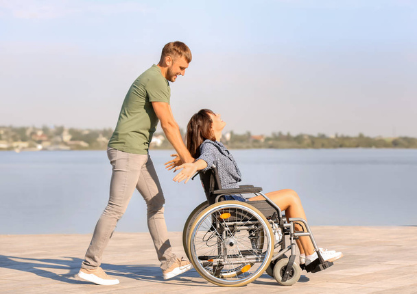 ευτυχισμένος νεαρή γυναίκα στο αναπηρικό αμαξίδιο και ο σύζυγός της κοντά στο ποτάμι - Φωτογραφία, εικόνα