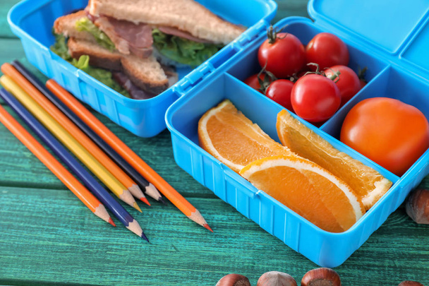 Caja de almuerzo con alimentos apetitosos y papelería en la mesa de madera de color
 - Foto, Imagen
