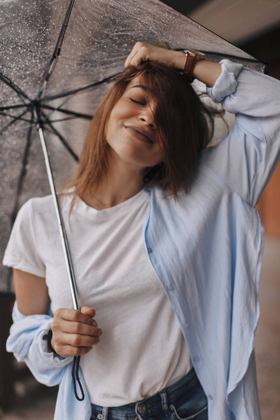 Mulher atraente sob o guarda-chuva usando camisa azul. A rapariga parece feliz. Chuva
 - Foto, Imagem