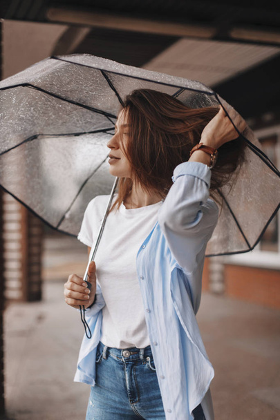 Attractive woman under the umbrella wearing blue shirt. Girl look happy. Rain - 写真・画像
