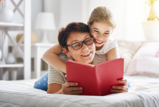 Grandmother reading a book to her granddaughter. Family holiday and togetherness. - 写真・画像
