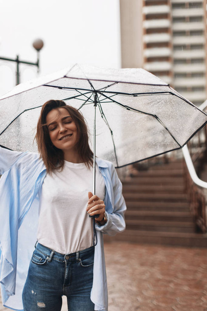 Ελκυστική γυναίκα κάτω από την ομπρέλα φοράει μπλε πουκάμισο. Κορίτσι φαίνονται ευχαριστημένοι. Βροχή - Φωτογραφία, εικόνα